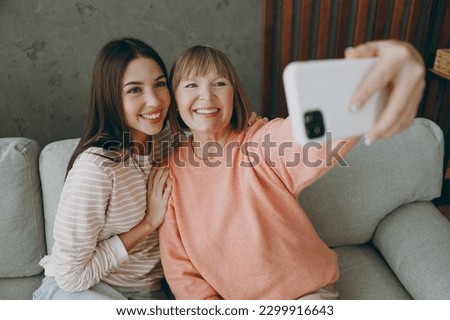 Two adult women mature mom young kid wear casual clothes doing selfie shot on mobile cell phone sit on gray sofa couch stay at home flat rest relax spend free spare time in living room. Family concept
