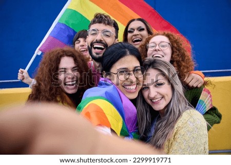 Selfie of a LGBT group of young people celebrating gay pride day holding rainbow flag together. Homosexual community smiling and taking cheerful self portrait. Lesbian couple and friends generation z Royalty-Free Stock Photo #2299919771