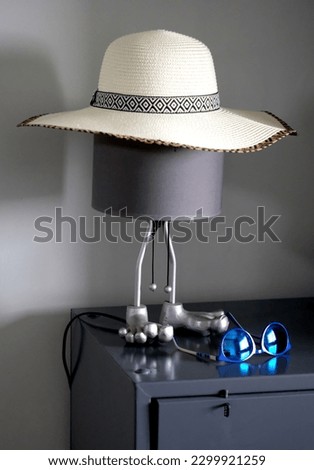 A hat resting on a bedside lamp with large metal legs and blue sunglasses shot with color saturation