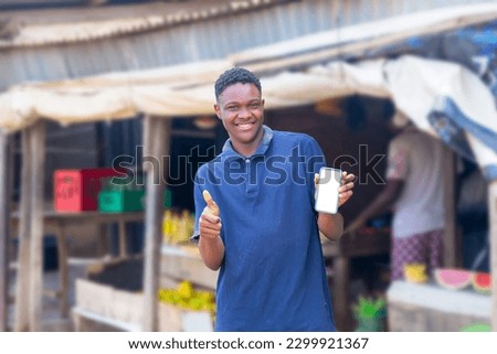copy space image of Young black man using his mobile phone and his thumbs up showing sign of approval, isolated in a local market