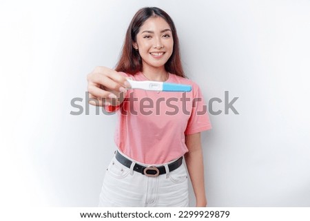 Happy young woman wearing pink t-shirt showing her pregnancy test and ultrasound picture, isolated on white background, pregnancy concept 