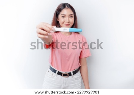 Happy young woman wearing pink t-shirt showing her pregnancy test and ultrasound picture, isolated on white background, pregnancy concept 