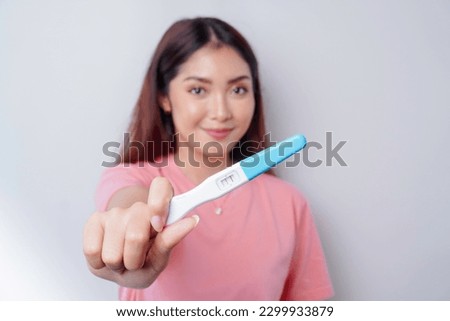 Happy young woman wearing pink t-shirt showing her pregnancy test, isolated on white background, pregnancy concept 