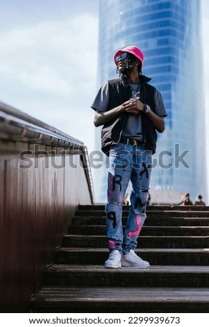 A sunny day captures a striking portrait of a casually dressed African boy, sporting a trendy pink cap, standing on a wooden runway with stairs Royalty-Free Stock Photo #2299939673