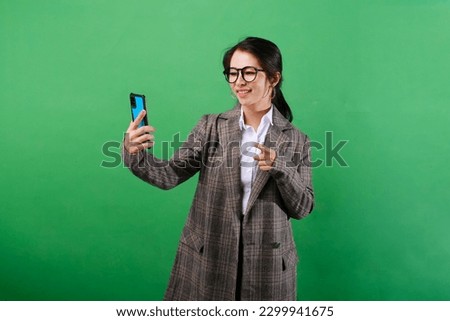 Photo of smiling Asian businesswoman showing mobile phone screen and OK hand sign gesture on isolated green background