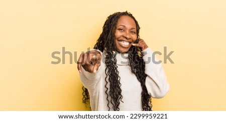 black pretty woman smiling cheerfully and pointing to camera while making a call you later gesture, talking on phone