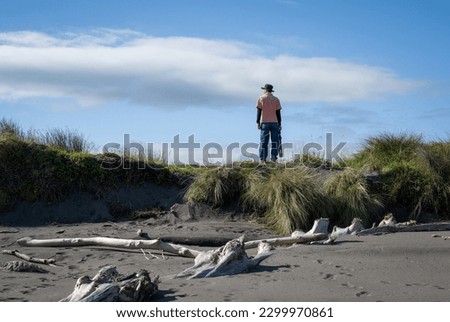 Man standing on the edge of the beach and holding a tripod. Photographer searching for photo locations. New Plymouth.