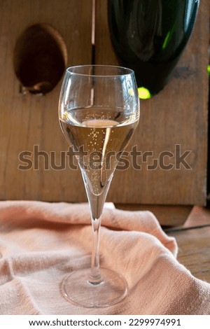 Glass of sparkling white wine champagne gran cru or cava with bubbles and classic wooden champagne pupitre rack with empty bottles on background