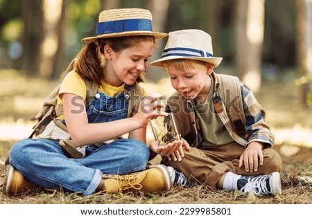 Two little children boy and girl with backpacks looking examine plants and collect herbarium in a glass jar while exploring forest nature and environment during outdoor ecology school lesson
 Royalty-Free Stock Photo #2299985801