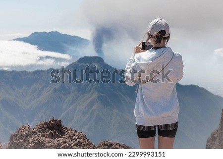 Tourist girl takes picture of Cumbre Vieja volcanic eruption on the island of La Palma, Canary Islands. Volcano La Palma from far aerial view.		