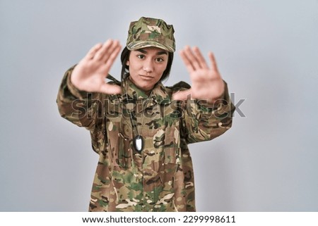 Young south asian woman wearing camouflage army uniform doing frame using hands palms and fingers, camera perspective 