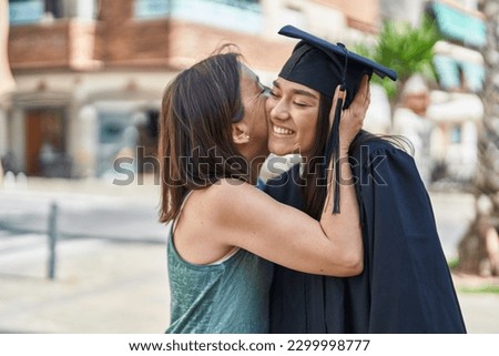Two women mother and graduated daughter kissing at street