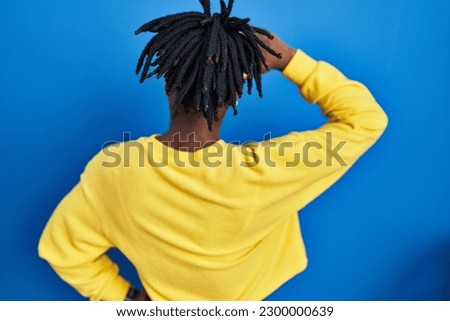Beautiful black woman standing over blue background backwards thinking about doubt with hand on head 
