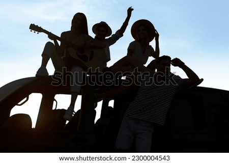 Friends with guitar and car chilling outdoors. Silhouettes of people against blue sky Royalty-Free Stock Photo #2300004543