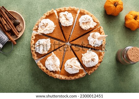 Traditional pumpkin pie for Thanksgiving cut into slices with whipped cream and leaf shaped decorations