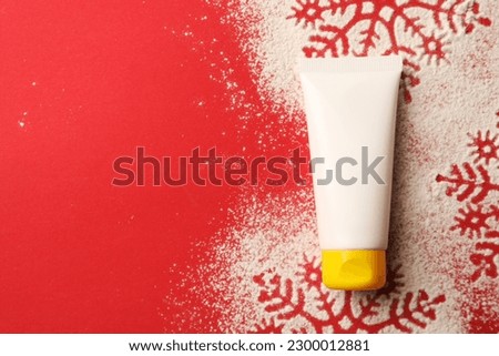 Winter skin care. Hand cream and snowflake silhouettes made with artificial snow on red background, top view. Space for text