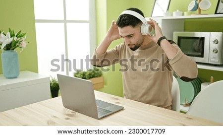 Young arab man using laptop and headphones sitting on table at home