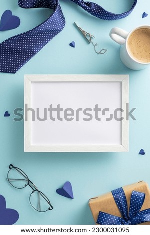 Father's Day surprise idea. A pastel blue background with top vertical view of coffee cup, necktie, spectacles, giftbox, and other men's accessories. Empty photo frame for text or your photo