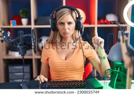 Young woman playing video games pointing up looking sad and upset, indicating direction with fingers, unhappy and depressed. 