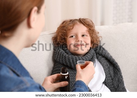 Mother giving cough syrup to her son on sofa Royalty-Free Stock Photo #2300036413