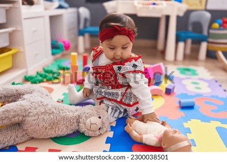 Adorable hispanic baby sitting on floor with relaxed expression at kindergarten