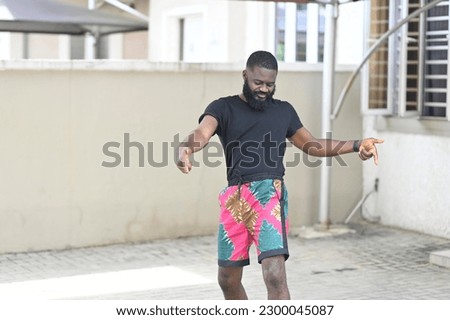 Young happy funky African American teen guy wearing ankara short having fun on the street. Smiling cool ethnic generation z teenager student model dancing and moving.
