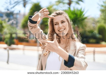 Young blonde woman smiling confident doing photo gesture with hands at park