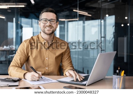 Portrait of young businessman in shirt, man smiling and looking at camera at workplace inside office, accountant with calculator behind paper work signing contracts and financial reports.