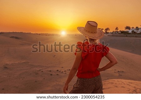 tourist woman wearing sunhat to shield herself from the sunset. she close her eyes and listen to the sound of ocean waves in the distance or watch as sand dunes shift and change shape in the breeze. Royalty-Free Stock Photo #2300054235