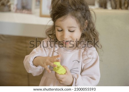 Caucasian child, two or three years old, playing and exercising fine motor skills with her hands, with clay and colored plasticine. Concept of happy childhood, learning and creativity. Copy space Royalty-Free Stock Photo #2300055593