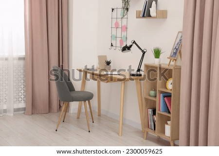 Stylish workplace with wooden desk, chair and lamp in room. Interior design Royalty-Free Stock Photo #2300059625