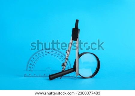 Protractor, magnifying glass and compass on light blue background