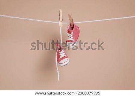 Cute small baby shoes hanging on washing line against brown background Royalty-Free Stock Photo #2300079995