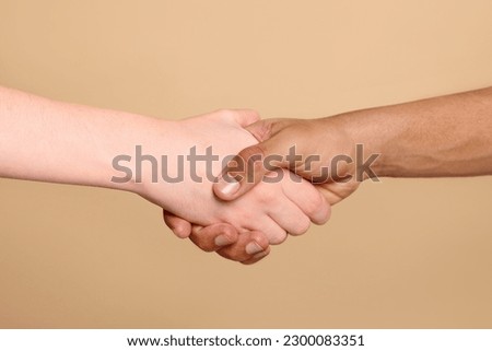 International relationships. People shaking hands on light brown background, closeup