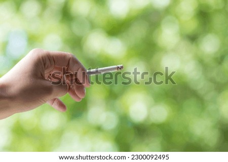 Close up view of a woman smoking a cigarette outdoors with focus ne her hand in defocused background with copy space. Female hand holding cigarette while consuming. tobacco concept