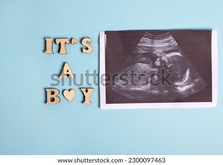 its a boy from wooden letters on blue background.baby infant toddler pacifier blanket ultrasound picture.white small heart meaning love care of fetus.baby awaiting.