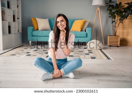 Photo of tricky cunning young girl wear pink t-shirt finger chin sitting floor legs crossed indoors home room Royalty-Free Stock Photo #2300102611