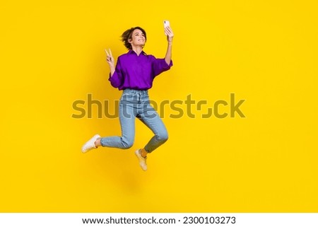 Full length photo of excited pretty woman dressed purple shirt jumping recording video vlog v-sign empty space isolated yellow color background