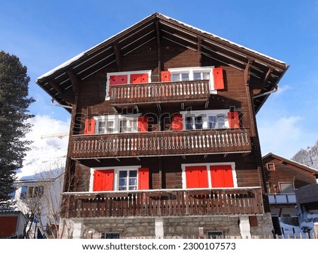 Traditional style wooden chalet with bright red shutters in Andermatt village in the Swiss Alps. Royalty-Free Stock Photo #2300107573