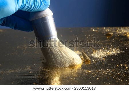 Person gilding a wooden table top with gold leaf sheets and a brush. Upcycling craft concept. Royalty-Free Stock Photo #2300113019
