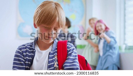 Sad bullied boy standing in classroom while three classmates behind him scoffing. Concept of discrimination and negative communication in society. Royalty-Free Stock Photo #2300116835