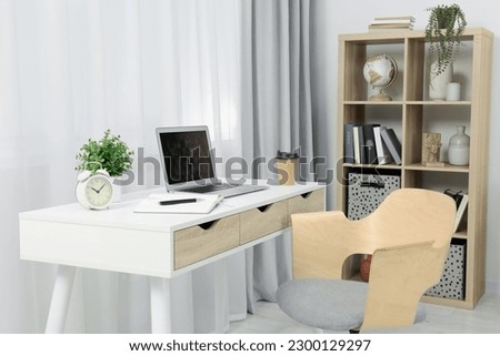 Workplace with modern laptop on desk and comfortable chair at home Royalty-Free Stock Photo #2300129297