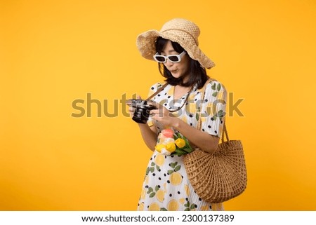 Studio portrait pretty young asian woman happy smile dressing springtime fashion with sunglasses, woven bag and holding tulip bouquet flower and camera against yellow studio background. Travel concept