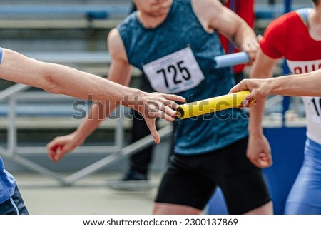 men relay race baton passing in summer athletics championship, close-up of athletes hands on background of runners Royalty-Free Stock Photo #2300137869