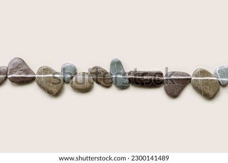Top view still life with close-up sea stones on sand background, pebbles united by one horizontal row. Row from natural stone natural tones. Minimal style flat lay, concept of calm, peace, meditation