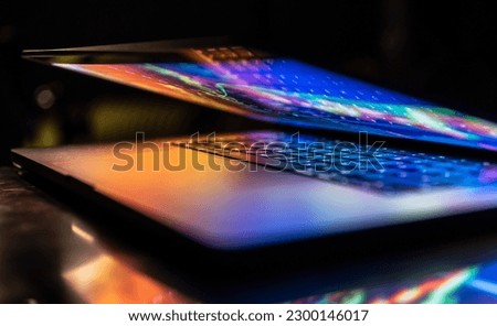 A laptop half closed in the dark with colourful glow.