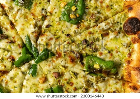 Pizza with sourdough dough, four cheeses with jalapenos and pistachios and parmesan cheese on top on a light ceramic plate. The dish stands on a light tablecloth next to a glass of white wine.