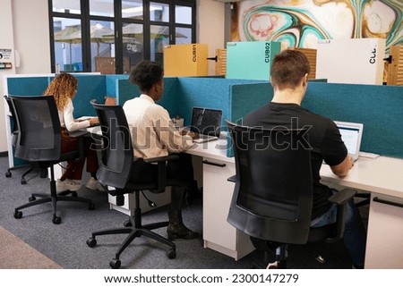 Three young people share coworking space, work side by side with desk dividers Royalty-Free Stock Photo #2300147279