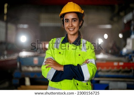 Portrait of Brazilian woman worker beautiful face with eye confident and wearing working suite dress and safety helmet at heavy machine in industry factory. Brazilian worker concentrate on workplace.