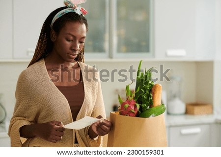 Young woman checking her shopping list after getting groceries delivered to her house Royalty-Free Stock Photo #2300159301